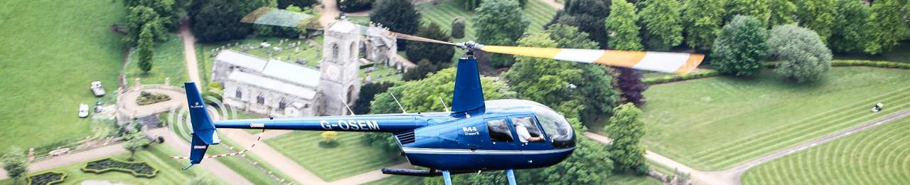 A blue helicopter flying over a church and grounds.